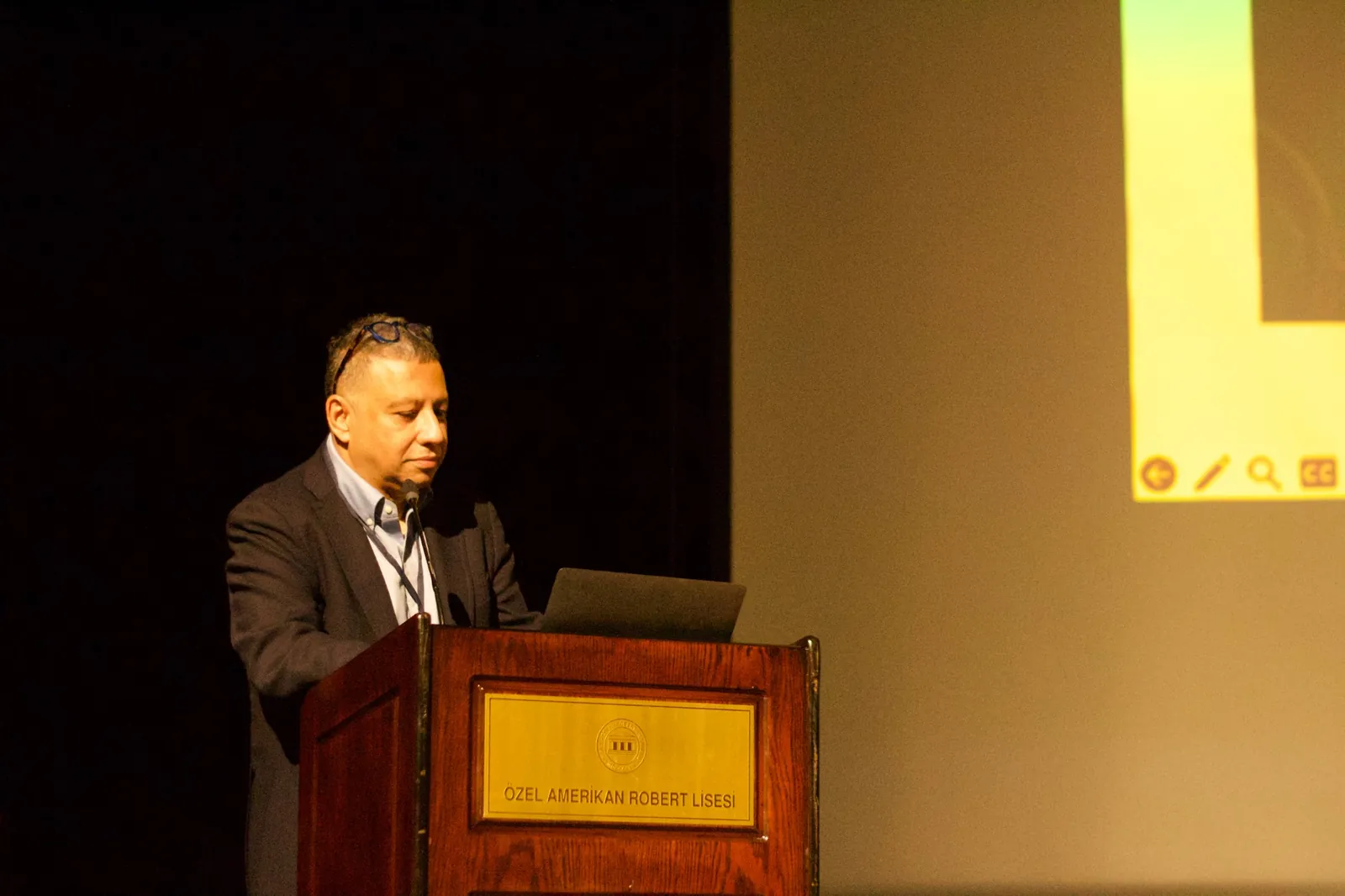 A speaker at the lectern, with slides projected on the screen behind him